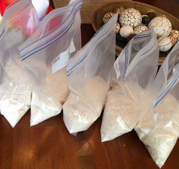Five Ziploc bags of white rice sitting on a brown tabletop.