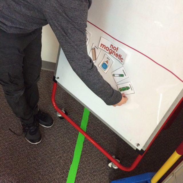 Student is bending over a white board placing small cards under the title "not magnetic."