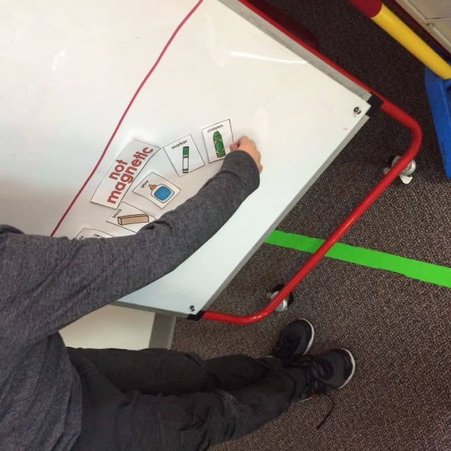 Student is bending over a white board placing small cards under the title "not magnetic."