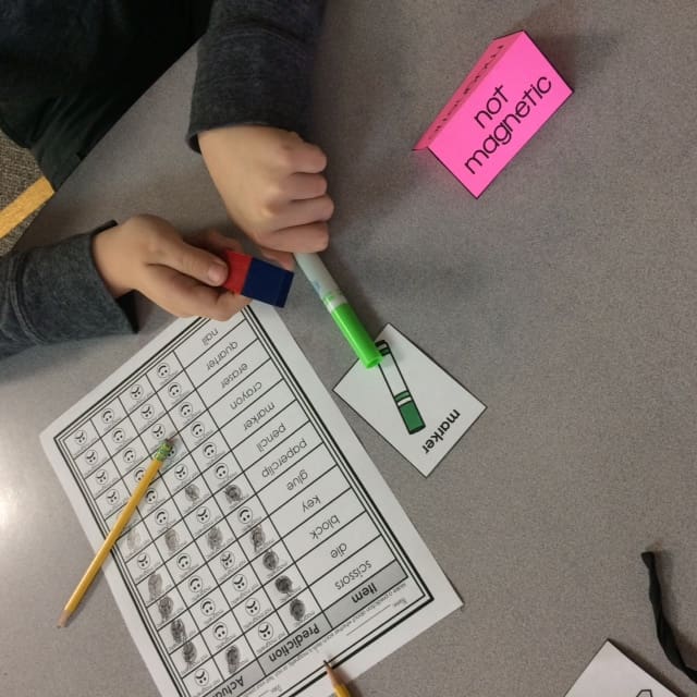 You can see the hands of a student using a green marker to predict if it is magnetic.
