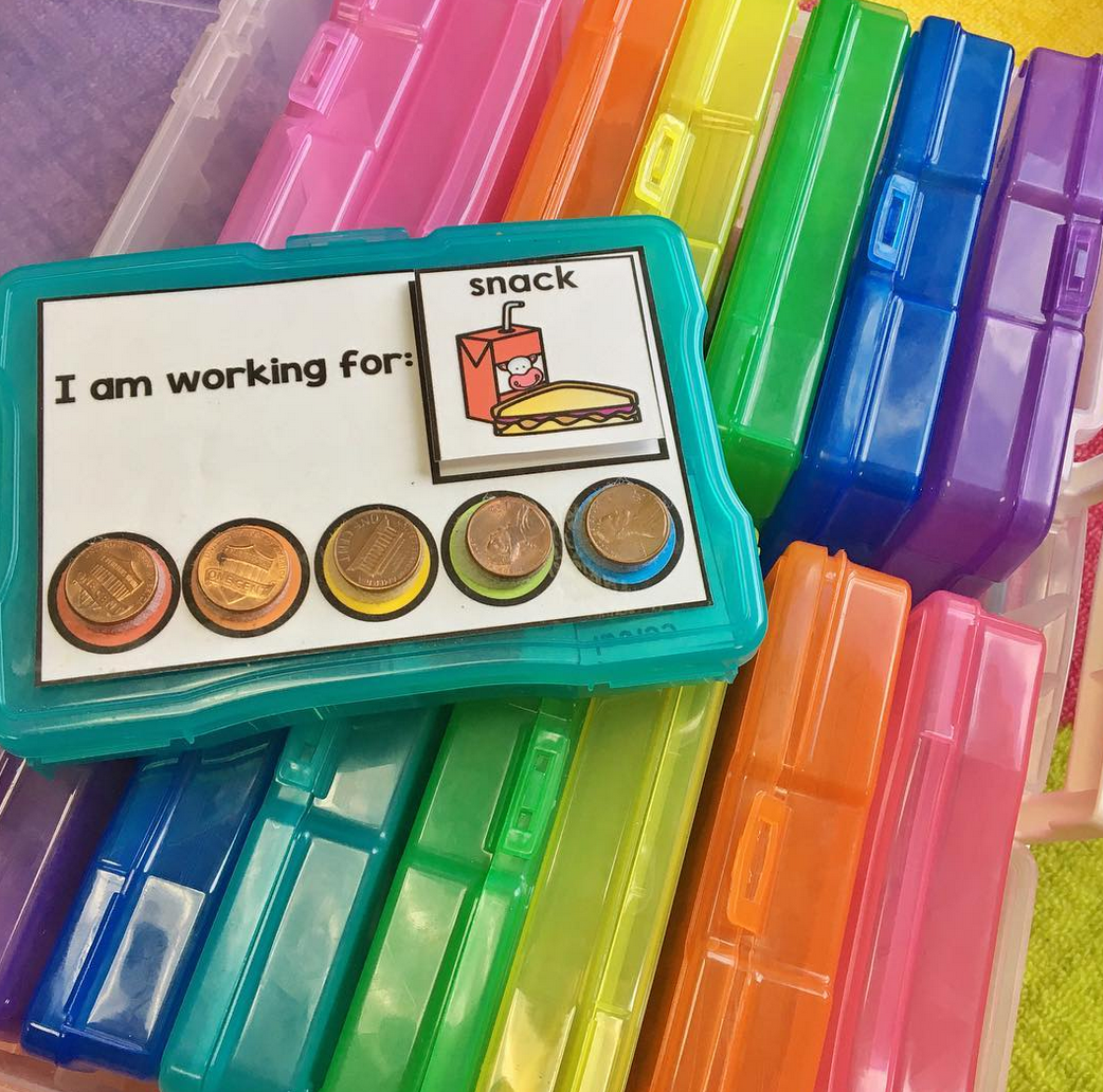A set of plastic boxes in a variety of rainbow colors. On top of the boxes sits a teal plastic box showing a reward and token sysytem.