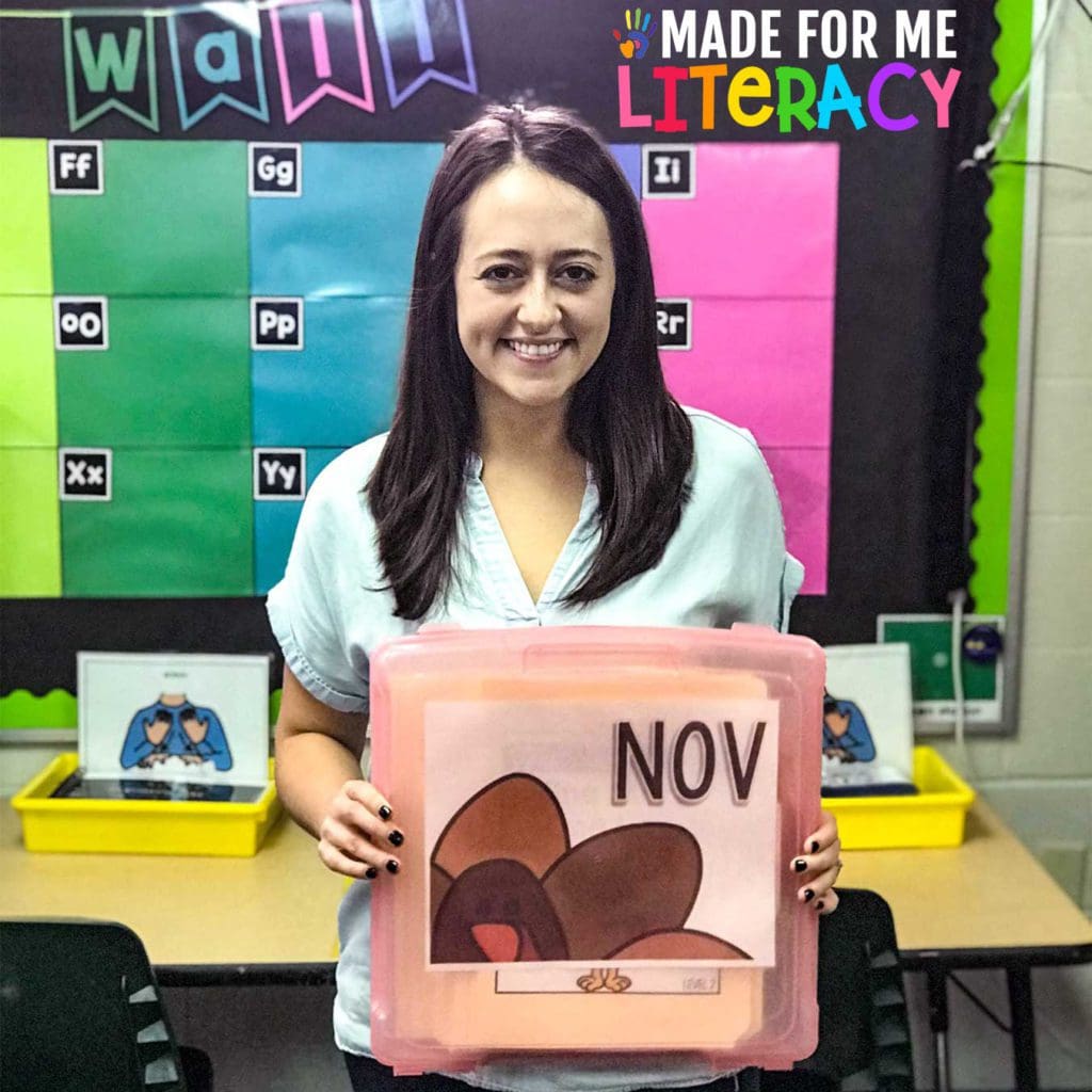 Smiling dark haired female teacher holding a clear pink container with her November turkey Made For Me Literacy teaching materials