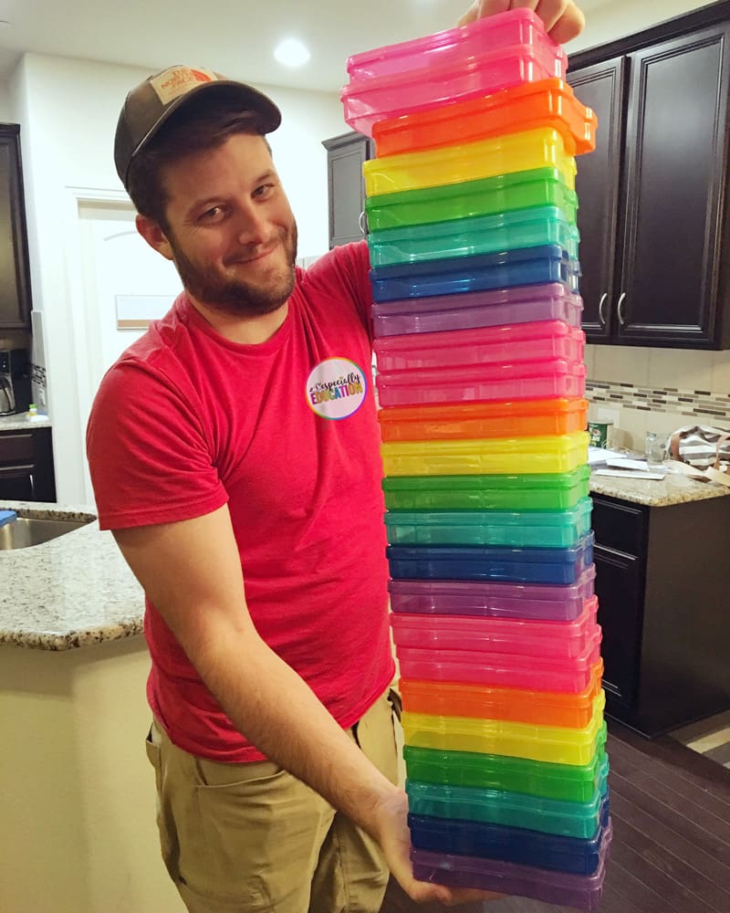Man in a red shirt holding a tall stack of colorful plastic boxes