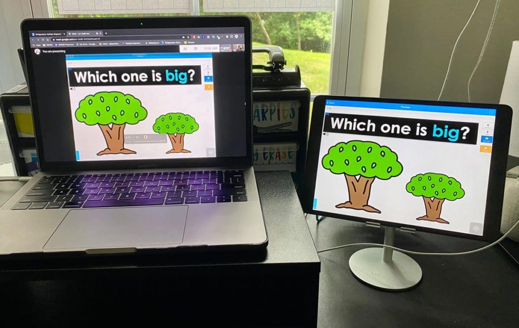 A special education teacher's laptop is connected to an iPad with both screens displaying a gamified Made For Me Literacy Boom Card for her distant learning students 