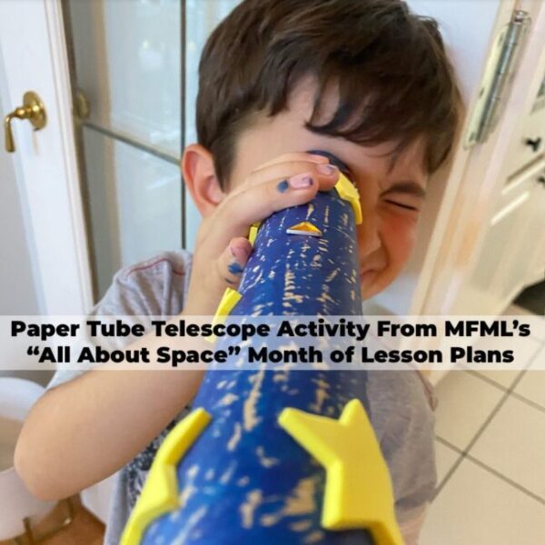 A young boy looking out of a cardboard play telescope he made himself painted blue with yellow stars.