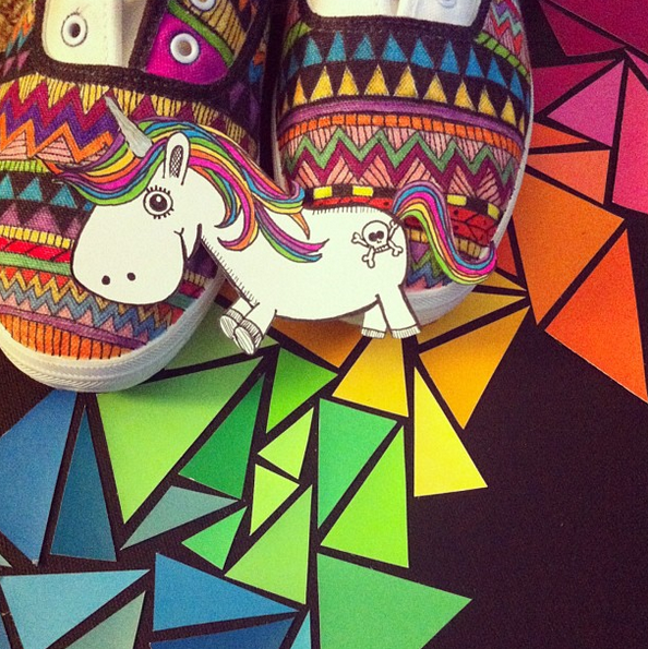 A pair of white tennis shoes that have been decorated with colorful geometic patterns, using fabric pens. A cutout of the Especially Education unicorn sits at the toes of the shoes.