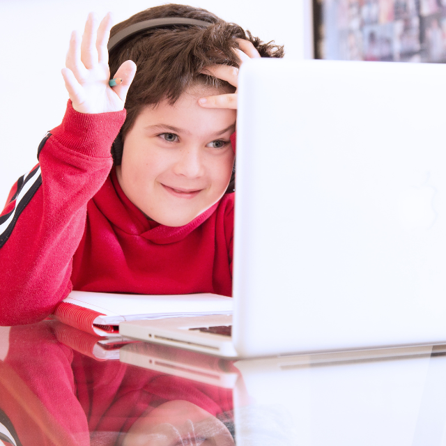 A smiling homeschooled child working on a laptop - waving at the screen.