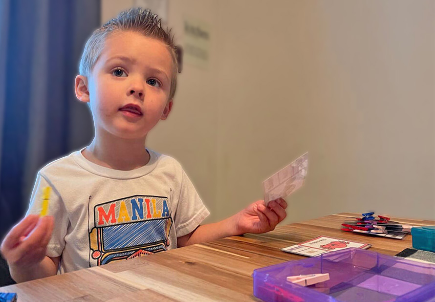 Young boy in a white t-shirt at the kitchen table working on a task box.