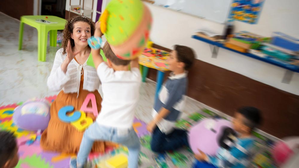 End of the year student chaos for a special education teacher. Children are not listening and a boy is throwing a stuffed ball at the teacher's head.
