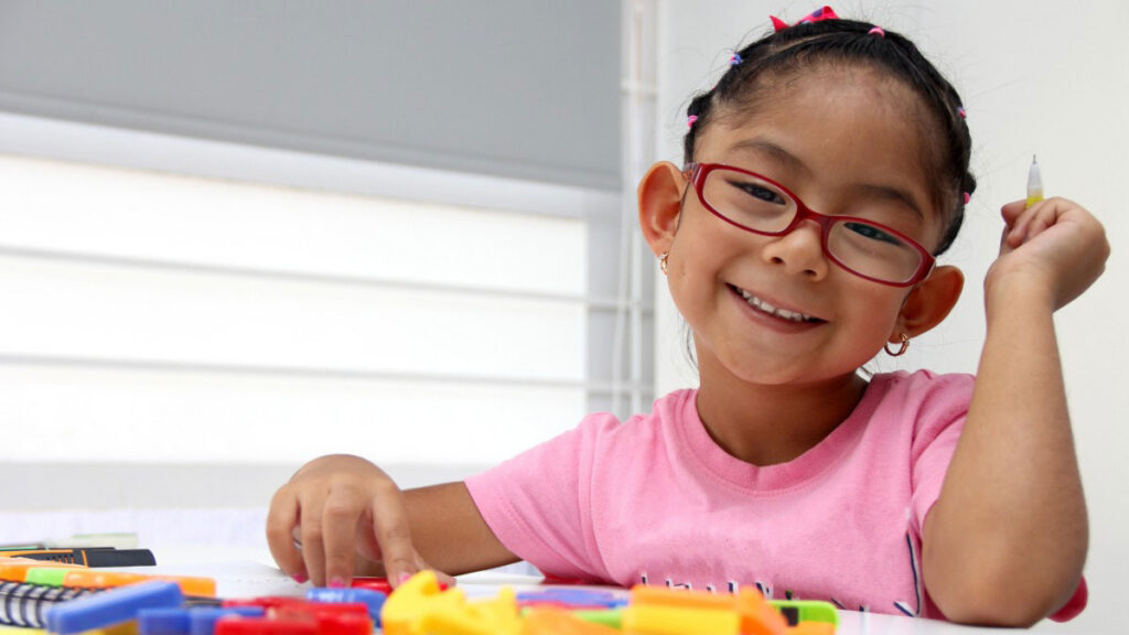 Young student smiling while completing a hands-on fine motor activity at a classroom table