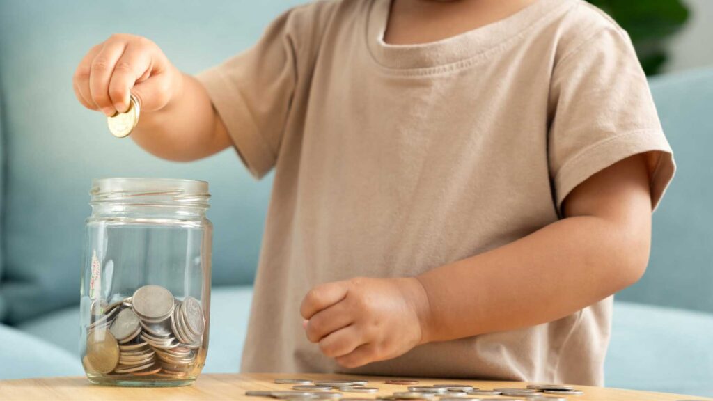 Preschool child dropping change into a jar learning to get used to money concepts